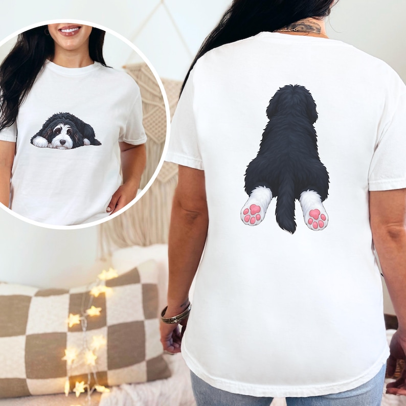 May include: White t-shirt featuring a black and white dog illustration on the front and back. The front shows the dog lying down, while the back displays the dog's rear with pink paw pads. A casual, comfortable tee.