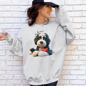 A woman wearing a Bernedoodle sweatshirt with cute design on the front and the back.  The front features a bernedoodle dog in claymation design holding a heart with his name, across the top of his head the words, "Doodle Mom".