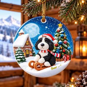 A decorative ornament featuring a black and white dog wearing a Santa hat and scarf, sitting on a sled and looking out a window with a snowy landscape and a full moon in the background.