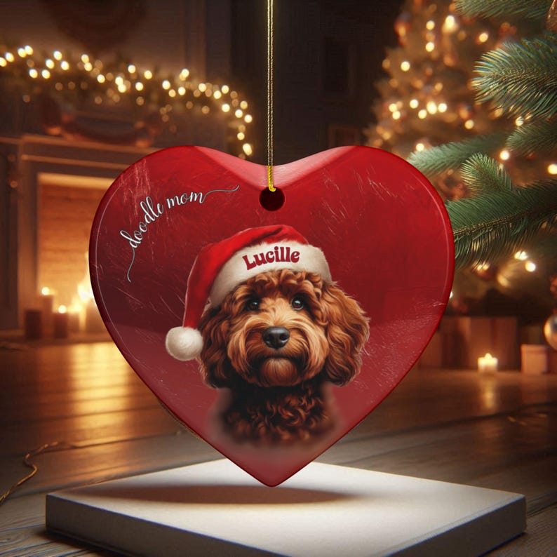 May include: Red heart-shaped Christmas ornament featuring a brown Doodle dog wearing a Santa hat with the name "Lucille." The ornament has the words "doodle mom" in script. A gold string is attached for hanging.
