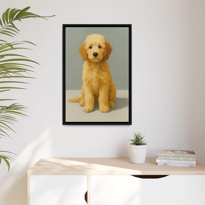 May include: A framed art print featuring a golden doodle dog. The dog is depicted in a seated position with a light yellow-orange coat and floppy ears. The artwork is set against a muted green background, with a neutral-colored surface below the dog. The frame is black.