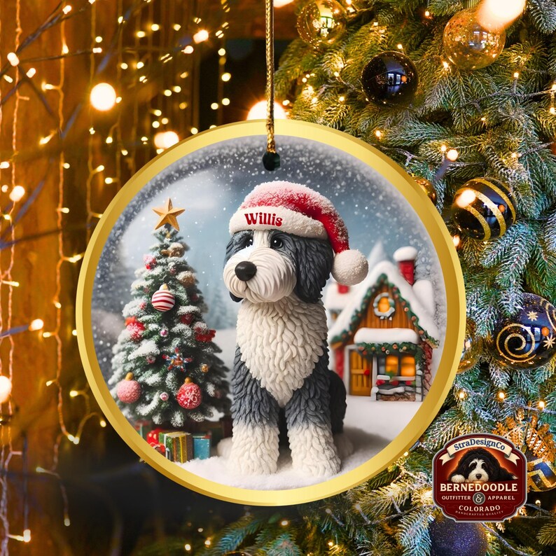 May include: A circular Christmas decoration with a gold edge. It features a dog wearing a Santa hat with the name "Willis" in a snowy scene with a Christmas tree and a house. The ornament hangs from a gold string.