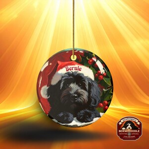 A black bernedoodle dog wearing a santa hat that is personalized with their name on it in this adorable Ceramic ornament!  Design appears on the front and the back of this doodle dog ornament!