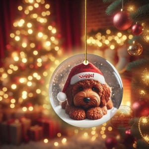 This ceramic ornament features a cute red mini-doodle golden doodle or goldendoodle dog wearing a Santa hat in a snow globe setting, surrounded by holiday decorations. Perfect for adding a festive touch to your Christmas tree or as a thoughtful gift for dog lovers.