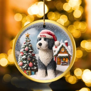 May include: A circular Christmas decoration with a dog wearing a Santa hat, the name "Willis" is visible. The ornament has a gold edge and shows a snowy scene with a Christmas tree and a house.