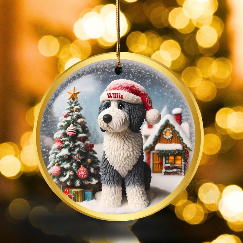 May include: A circular Christmas decoration with a dog wearing a Santa hat, the name "Willis" is visible. The ornament has a gold edge and shows a snowy scene with a Christmas tree and a house.