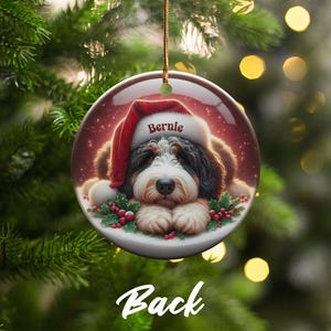 Personalize your holiday decor with this charming Bernedoodle Christmas ornament! Featuring a cute Bernedoodle in a festive Santa hat and customizable name, this round ornament adds warmth and joy to any tree. Perfect for dog lovers and unique gifts!