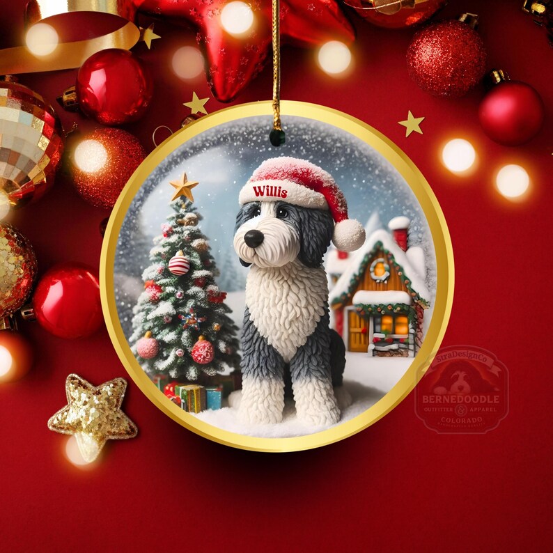 May include: A circular Christmas decoration with a gold edge depicts a dog in a Santa hat, with the name "Willis". A decorated Christmas tree and a snow-covered house are in the background. The ornament hangs against a red backdrop with festive decorations.