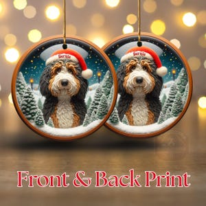 Op de afbeelding: Twee ronde kerstversieringen met een Bernedoodle-hond met een kerstmuts met de naam "Bernie". De ornamenten hebben een winterse achtergrond met besneeuwde bomen. De tekst "Front & Back Print" staat onderaan.