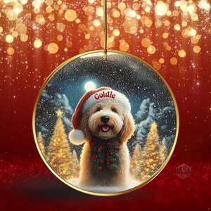 May include: A Christmas ornament featuring a fluffy dog wearing a Santa hat with the name "Goldie" and a festive green and red garland. The background shows a snowy forest scene inside a gold-rimmed circle, with a red and gold bokeh effect.