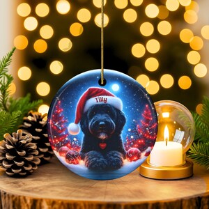 This festive ornament features an adorable black doodle wearing a Santa hat, surrounded by soft glowing holiday lights and rich red Christmas tones. The warm lighting highlights the dog’s fluffy black fur, giving the design a bright, cheerful look that stands out on any tree. A perfect personalized keepsake for anyone who loves black doodles and joyful holiday décor.