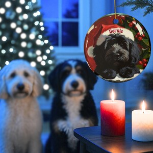 A black bernedoodle dog wearing a santa hat that is personalized with their name on it in this adorable Ceramic ornament!  Design appears on the front and the back of this doodle dog ornament!