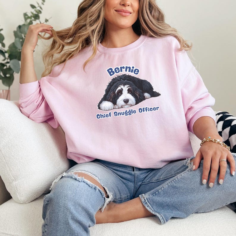Puede incluir: Una sudadera rosa claro con un gr&aacute;fico de un perro blanco y negro, el nombre "Bernie" arriba y "Chief Snuggle Officer" abajo. La sudadera tiene mangas largas.
