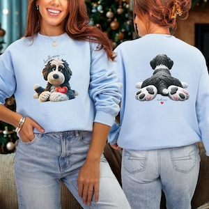 Puede incluir: Sudadera azul claro con un gráfico de un perro blanco y negro con un corazón rojo que dice "BAMBIE". La parte delantera de la sudadera tiene el texto "doodle mom". La parte trasera de la sudadera tiene un gráfico del trasero del perro.