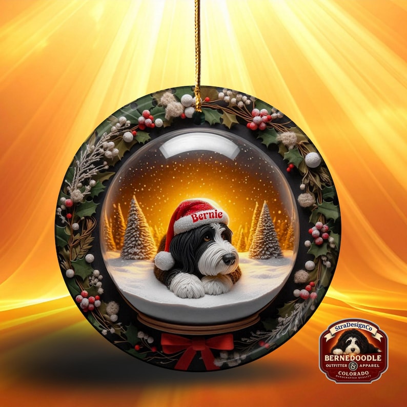 May include: A round Christmas ornament featuring a snow globe design. Inside the globe is a black and white dog wearing a Santa hat with the name "Bernie". The ornament is decorated with holly and berries, and has a red bow at the bottom.