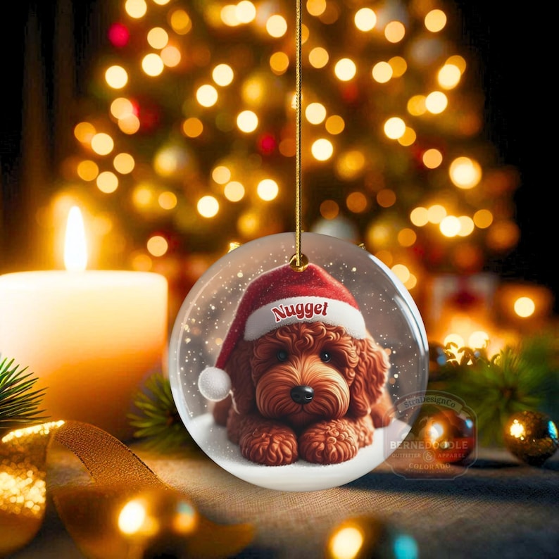This ceramic ornament features a cute red mini-doodle golden doodle or goldendoodle dog wearing a Santa hat in a snow globe setting, surrounded by holiday decorations. Perfect for adding a festive touch to your Christmas tree or as a thoughtful gift for dog lovers.