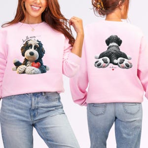 A woman wearing a Bernedoodle sweatshirt with cute design on the front and the back.  The front features a bernedoodle dog in claymation design holding a heart with his name, across the top of his head the words, "Doodle Mom", on the back, it shows the bernedoodle laying rear view with the pads of his doodle feet flipped back in a cute pose, with a heart and the words, "Doodle Mom".
