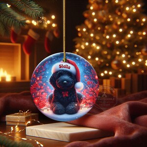Capture the magic of the season with this adorable black Goldendoodle puppy wearing a festive Santa hat, surrounded by glowing red berries and twinkling snowflakes! Perfect personalized Christmas tree ornament for doodle parents. Add your dog's name (like "Stella") for a heartfelt touch. High-quality ceramic, vibrant print, gold string included. Ideal dog mom/dad gift, stocking stuffer, or memorial keepsake. Handmade holiday charm!