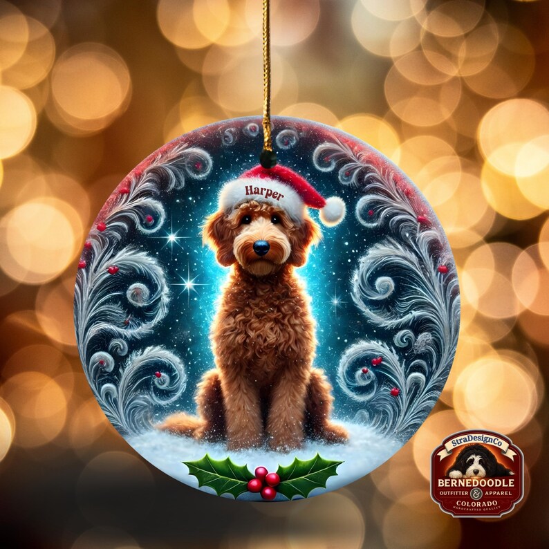 Christmas ornament with an illustrated goldendoodle wearing a Santa hat labeled “Harper.” The round ceramic piece features swirling frosted textures, glowing snowflakes, deep blue night sky, and holly berries at the base. Warm bokeh holiday lights shine behind the ornament, making it ideal for festive décor and personalized pet-themed gifts.