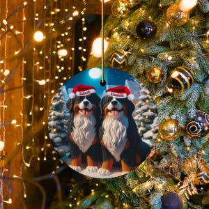 Op de afbeelding: Een ronde kerstversiering met twee Berner Sennenhonden met kerstmutsen. De honden heten "Edison" en "Einstein" op hun mutsen. De versiering hangt voor een versierde kerstboom met gouden en zwarte ballen.