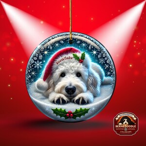 May include: A round Christmas ornament featuring a white dog wearing a Santa hat with the word "Snowflake". The ornament has a winter scene with snowflakes and holly. The background is red with spotlights.