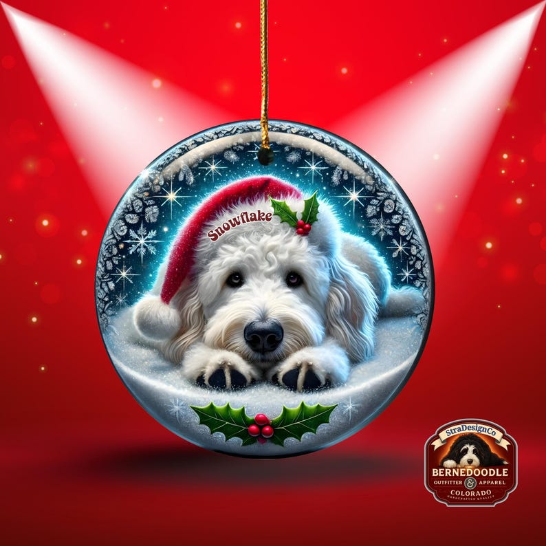 May include: A round Christmas ornament featuring a white dog wearing a Santa hat with the word "Snowflake". The ornament has a winter scene with snowflakes and holly. The background is red with spotlights.