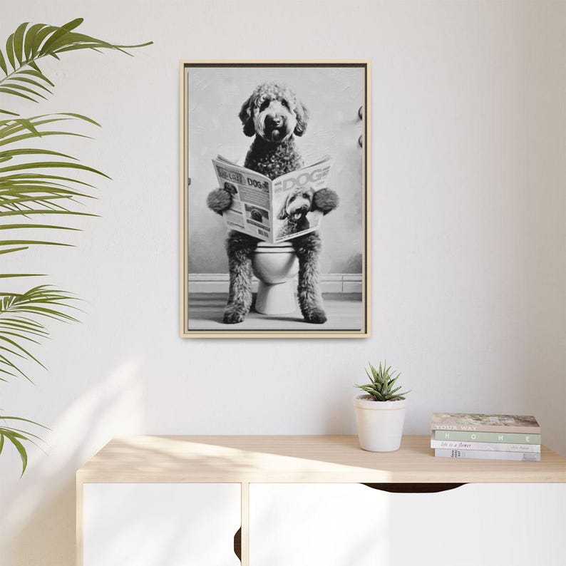 May include: A black and white framed wall art print featuring a curly-haired dog sitting on a toilet while reading a newspaper titled DOG. The dog is positioned upright, holding the open newspaper with both front paws, centered in the frame.