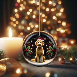 May include: A round Christmas ornament featuring a Goldendoodle wearing a Santa hat. The ornament has a black background with holly and berries, and the dog's name, "Goldie," is on the hat. The ornament hangs from a gold string.