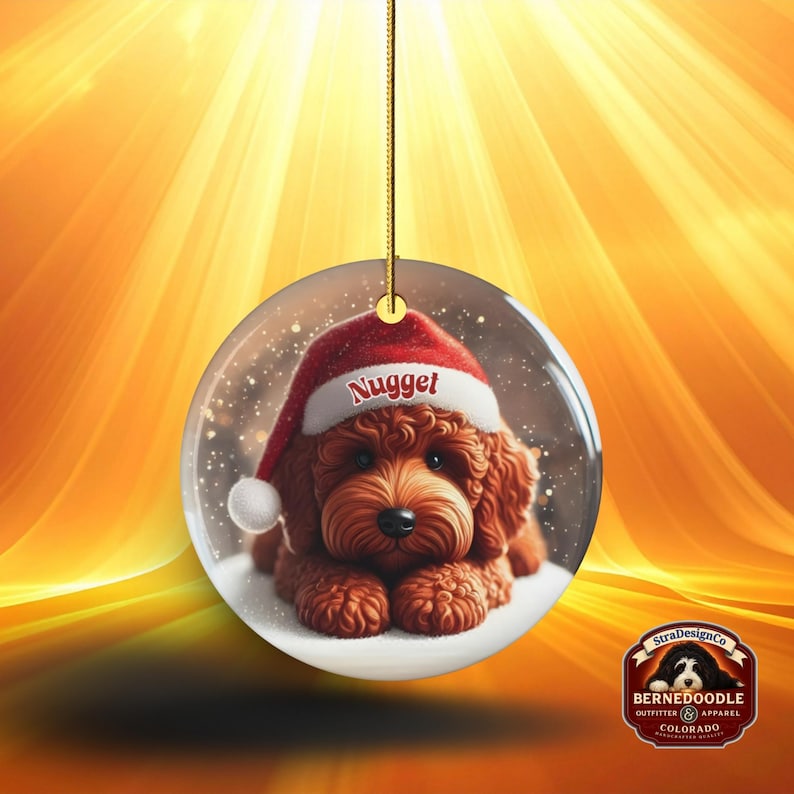 This ceramic ornament features a cute red mini-doodle golden doodle or goldendoodle dog wearing a Santa hat in a snow globe setting, surrounded by holiday decorations. Perfect for adding a festive touch to your Christmas tree or as a thoughtful gift for dog lovers.