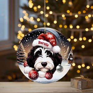 Personalize your holiday decor with this charming Bernedoodle Christmas ornament! Featuring a cute Bernedoodle in a festive Santa hat and customizable name, this round ornament adds warmth and joy to any tree. Perfect for dog lovers and unique gifts!