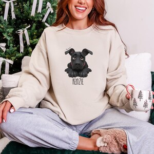 Puede incluir: Sudadera color crema con una ilustraci&oacute;n de un perro negro y el nombre "KENZIE" debajo. El perro tiene un collar rojo. La sudadera es de corte holgado, perfecta para uso casual.