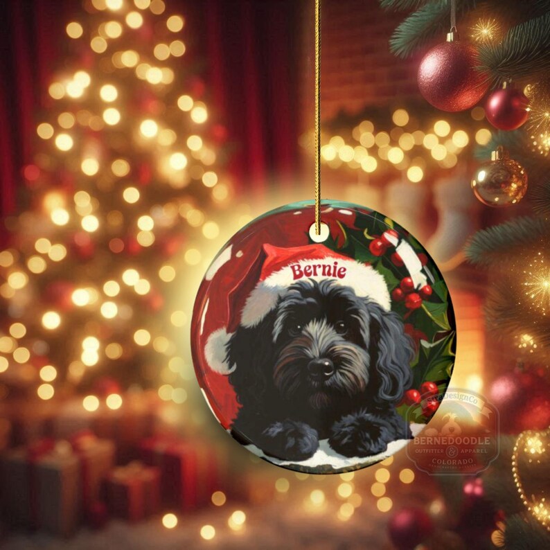 A black bernedoodle dog wearing a santa hat that is personalized with their name on it in this adorable Ceramic ornament!