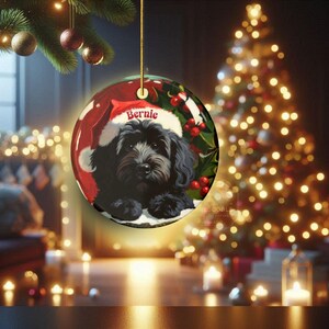 A black bernedoodle dog wearing a santa hat that is personalized with their name on it in this adorable Ceramic ornament!  Design appears on the front and the back of this doodle dog ornament!