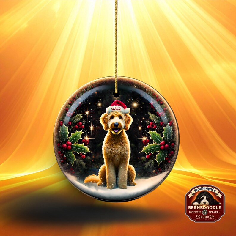 May include: A round Christmas ornament featuring a golden doodle dog wearing a Santa hat with the name "Goldie". The ornament is decorated with holly and berries, set against a starry night background. A gold string is attached for hanging.