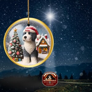 May include: A circular Christmas decoration showing a Bernedoodle dog in a Santa hat, with the name "Willis" on the hat. The ornament has a gold edge and features a Christmas tree and a snow-covered house. It hangs against a starry backdrop.