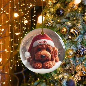 This ceramic ornament features a cute red mini-doodle golden doodle or goldendoodle dog wearing a Santa hat in a snow globe setting, surrounded by holiday decorations. Perfect for adding a festive touch to your Christmas tree or as a thoughtful gift for dog lovers.
