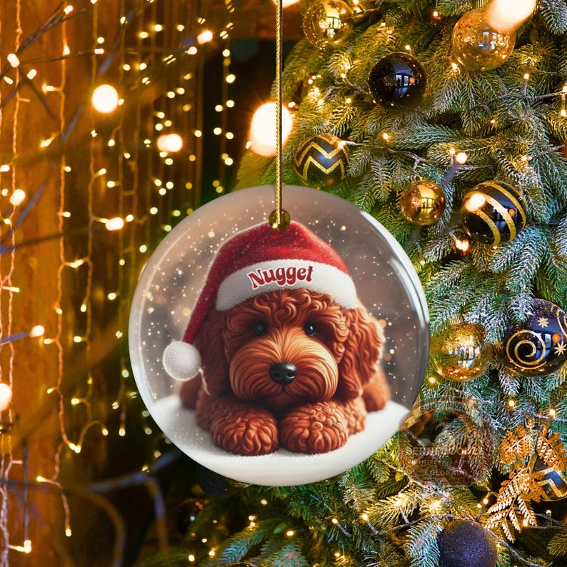 This ceramic ornament features a cute red mini-doodle golden doodle or goldendoodle dog wearing a Santa hat in a snow globe setting, surrounded by holiday decorations. Perfect for adding a festive touch to your Christmas tree or as a thoughtful gift for dog lovers.