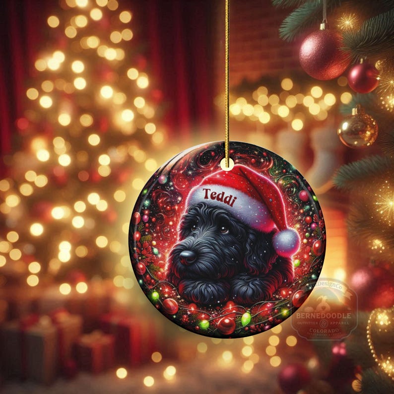 May include: A round Christmas ornament featuring a black dog wearing a Santa hat with the name "Teddi". The ornament is decorated with Christmas lights and a festive background. The ornament is hanging from a gold string.