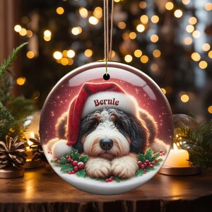 Personalize your holiday decor with this charming Bernedoodle Christmas ornament! Featuring a cute Bernedoodle in a festive Santa hat and customizable name, this round ornament adds warmth and joy to any tree. Perfect for dog lovers and unique gifts!
