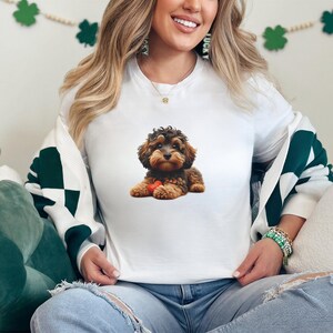 A woman wearing a white t-shirt with a dog image is sitting on a couch, smiling.