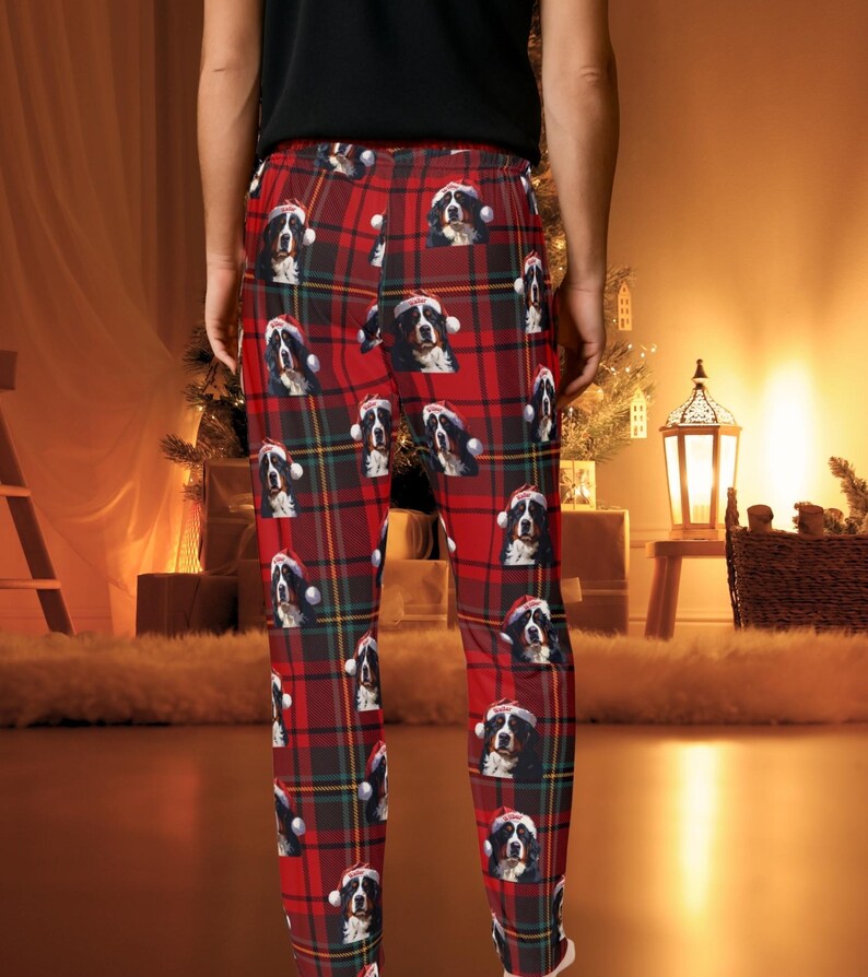 A man seen wearing Men's pajama pants lounge wear personalized Christmas pajama bottoms with Bernese Mountain dogs wearing Santa Hat and their name is on the Santa Hat.  Bernese Mountain Dog dad gear!