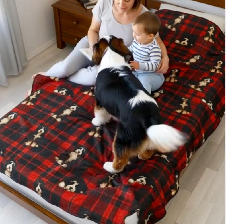 Peut inclure: Une couverture douce et moelleuse orn&eacute;e d'un motif &agrave; carreaux rouge et noir avec une impression r&eacute;p&eacute;titive de petites illustrations de chiens. La couverture est pos&eacute;e sur un lit, mettant en valeur la texture du tissu et les graphismes canins.