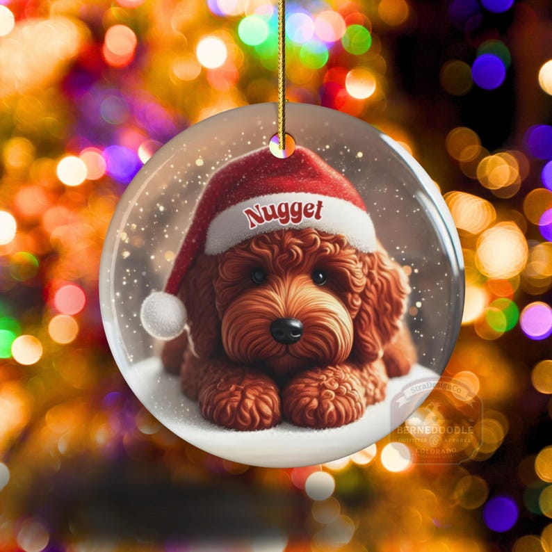 This ceramic ornament features a cute red mini-doodle golden doodle or goldendoodle dog wearing a Santa hat in a snow globe setting, surrounded by holiday decorations. Perfect for adding a festive touch to your Christmas tree or as a thoughtful gift for dog lovers.