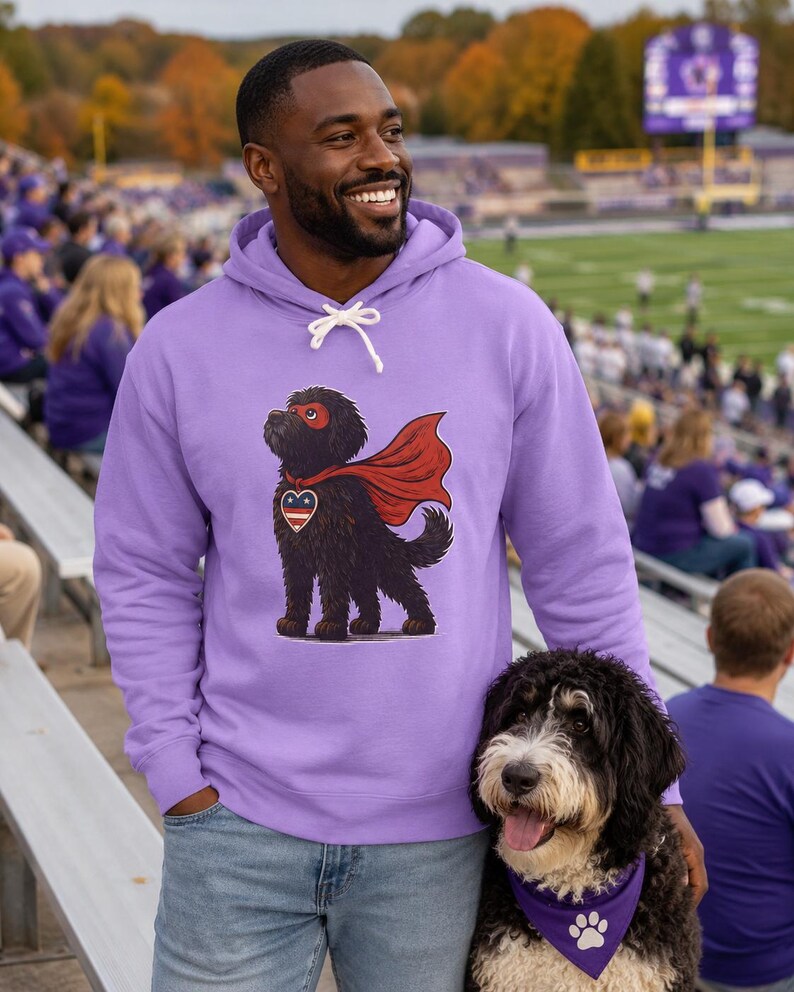 Pu&ograve; includere: Una felpa con cappuccio color viola chiaro con la grafica di un cane nero che indossa un mantello da supereroe rosso e una maschera rossa, con un emblema a forma di cuore sul petto con un motivo a stelle rosso, bianco e blu.