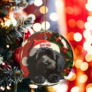 A black bernedoodle dog wearing a santa hat that is personalized with their name on it in this adorable Ceramic ornament!  Design appears on the front and the back of this doodle dog ornament!