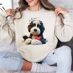 A woman wearing a Bernedoodle sweatshirt with cute design on the front and the back.  The front features a bernedoodle dog in claymation design holding a heart with his name, across the top of his head the words, "Doodle Mom".