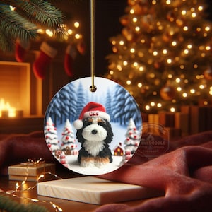Bernedoodle claymation style ornament made of ceramic, hanging by a gold string.  Winter scene featuring a cute, personalized doodle dog with personalized name on santa hat.  Perfect gift for Bernedoodle Dog Lovers and Pet Enthusiasts.