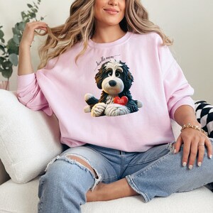 A woman wearing a Bernedoodle sweatshirt with cute design on the front and the back.  The front features a bernedoodle dog in claymation design holding a heart with his name, across the top of his head the words, "Doodle Mom".