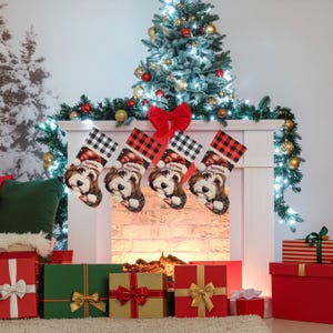 A festive Christmas stocking featuring a whimsical illustrated doodle dog wearing a red Santa hat, surrounded by holiday ornaments and greenery in a warm, detailed Christmas art style. The top of the stocking has a classic red and black buffalo-plaid cuff, and the stocking hangs from a white mantel decorated with evergreen garland and gold ornaments. The stocking design is personalized with your dog’s name, making it a charming and custom holiday décor piece for dog lovers.