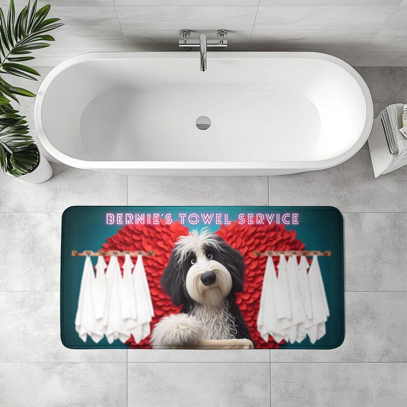 May include: A rectangular bath mat featuring a cartoon dog with black and white fur, and a long, white beard. The mat has the text "BERNIE'S TOWEL SERVICE" in pink neon. White towels hang on wooden rods on either side of the dog.